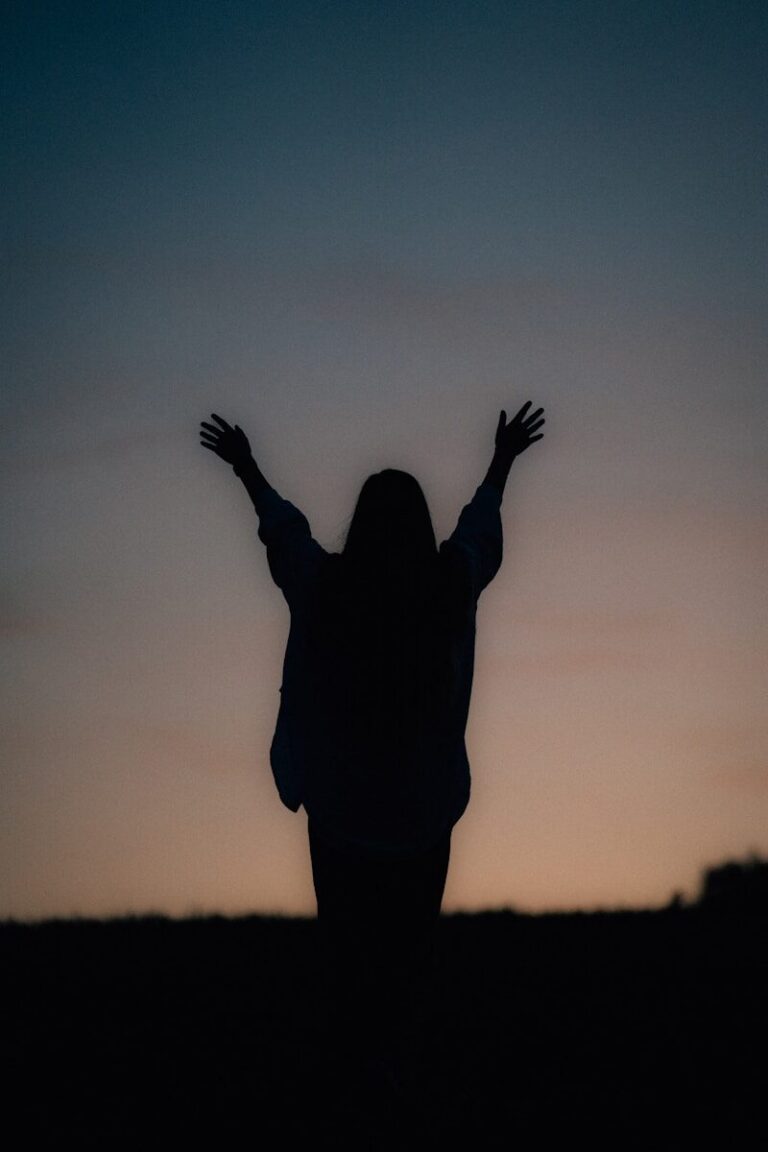 Silhouette of a person with arms raised at twilight.