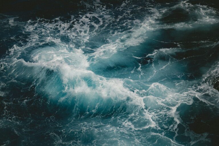 A turbulent blue ocean wave with white sea foam swirling in dark water