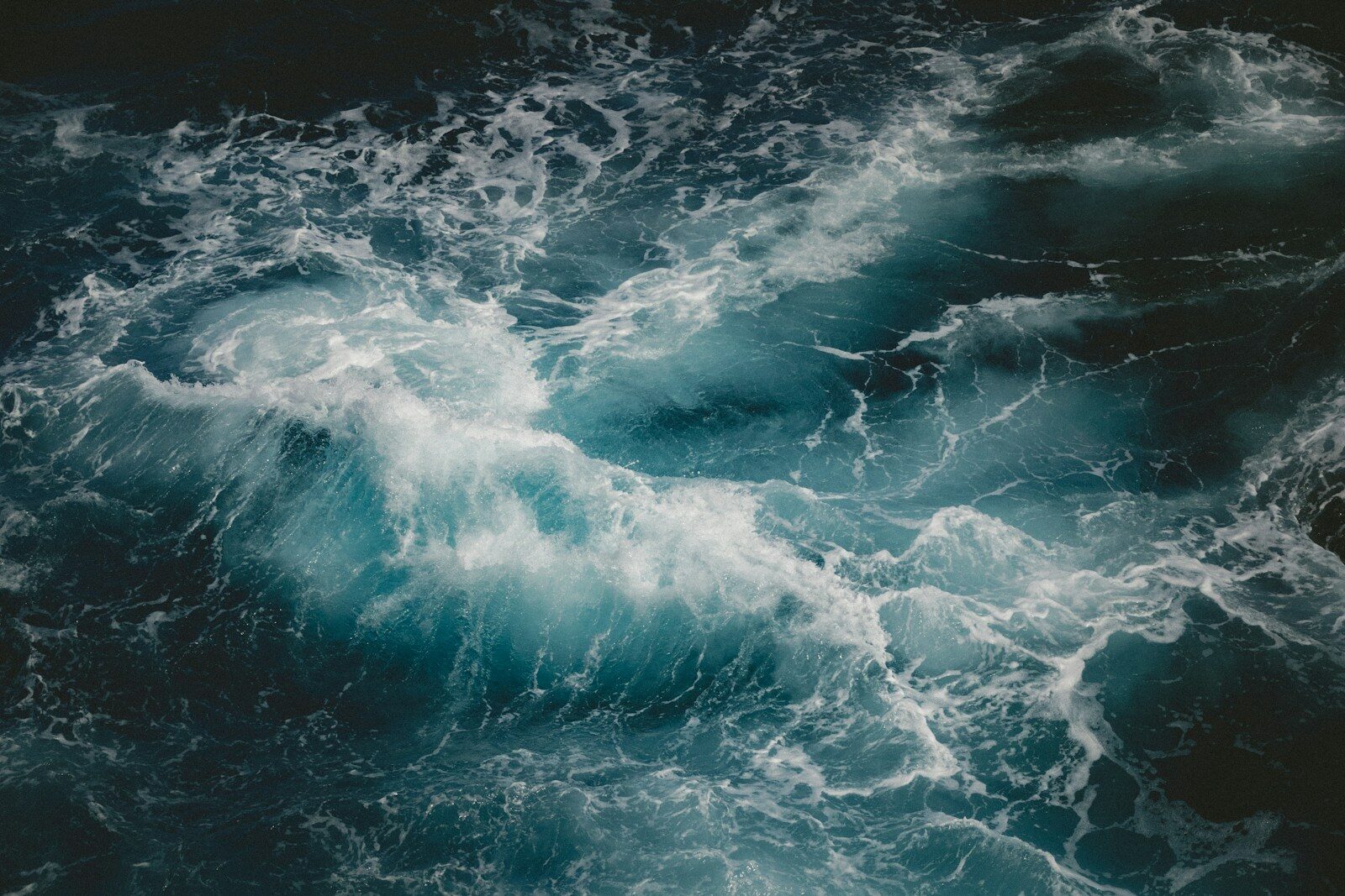A turbulent blue ocean wave with white sea foam swirling in dark water